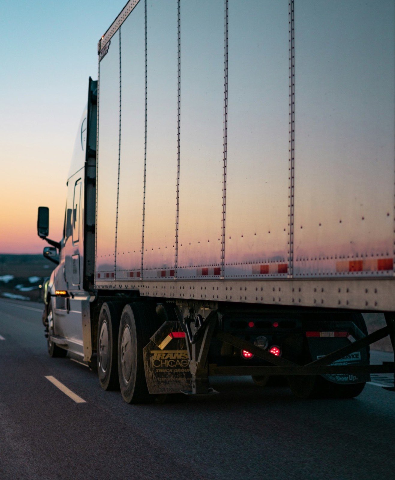 A freight truck on the highway at dusk, running a route.