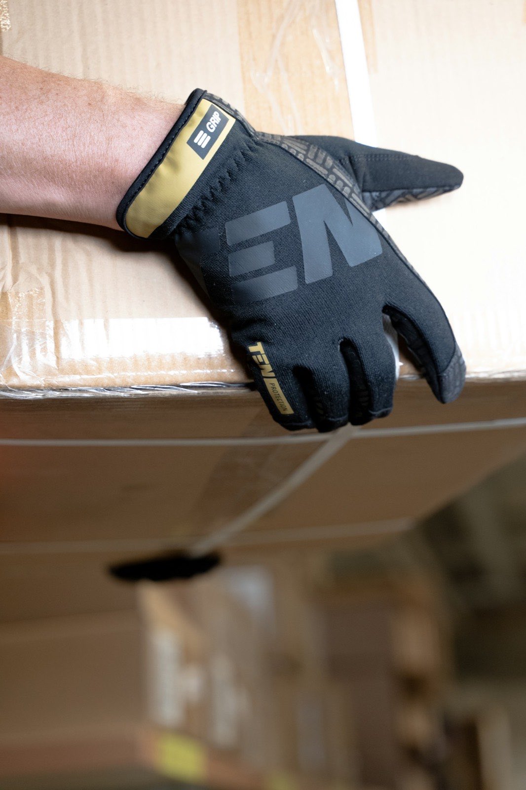 A gloved hand gripping the edge of a taped box — close on a crew member's hands at work.