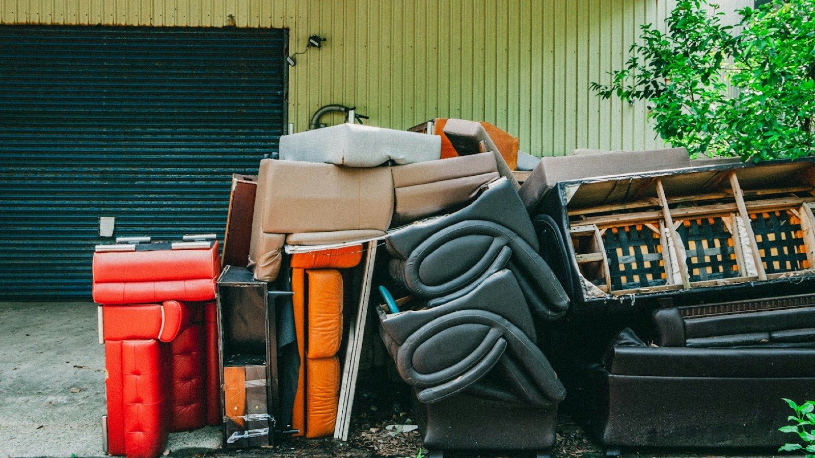 Sofas, chairs and a mattress stacked on a driveway, ready to be taken away.